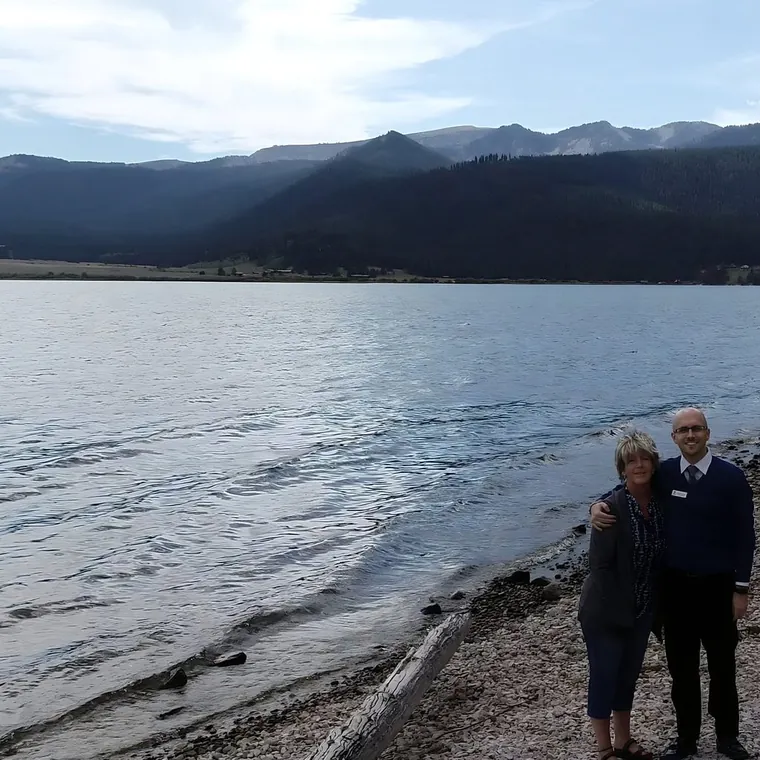 William Horschak and his mother on the shore of Lake Hebgen, with mountains across the water